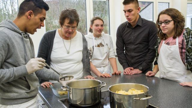 Saip Berisa erhitzt die russischen Teigtaschen. Mitschüler und Lehrerinnen lassen sich das Rezept erklären. Foto. SMMP/Bock